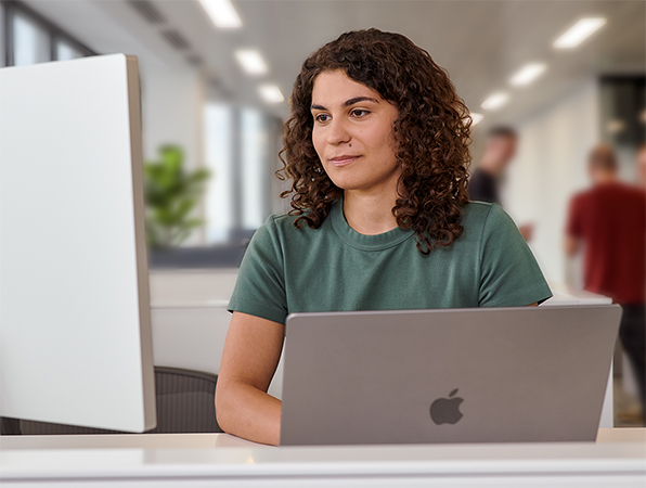 Członkini zespołu Apple pracująca w biurze na MacBooku z monitorem Studio Display.