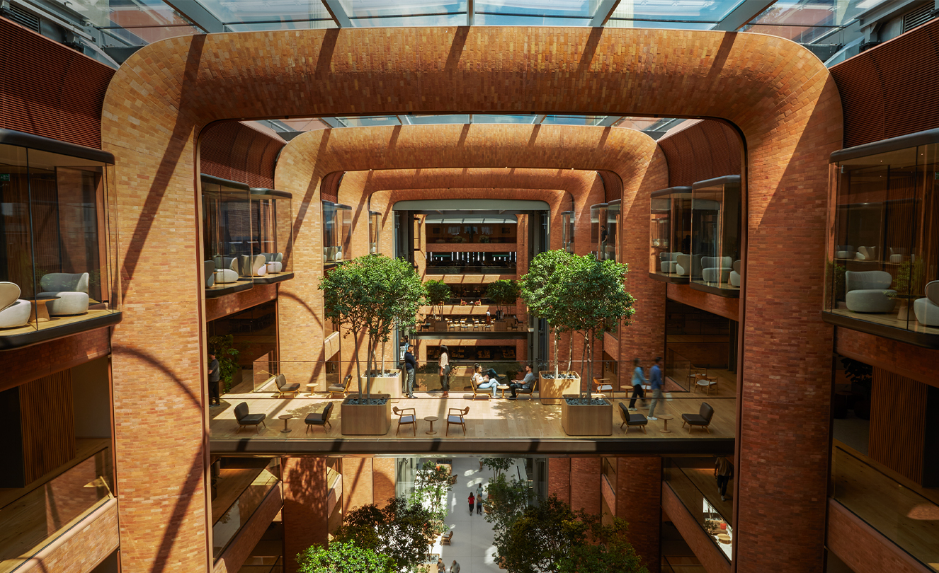 Pięciopoziomowe atrium w biurze Battersea. Promienie słońca wpadają przez szklany sufit i oświetlają pracowników poniżej.