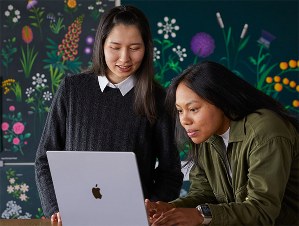 Deux membres de l’équipe Marketing d’Apple travaillent ensemble sur un MacBook devant des affiches conçues par leur équipe.