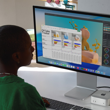 員工坐在 iMac 與 Mac mini 前，正在處理一份名為 「Q4 Sales Tracker」的 Excel 試算表。Excel 試算表後方是 Pixelmator Pro 視窗以及 macOS Tahoe 背景。