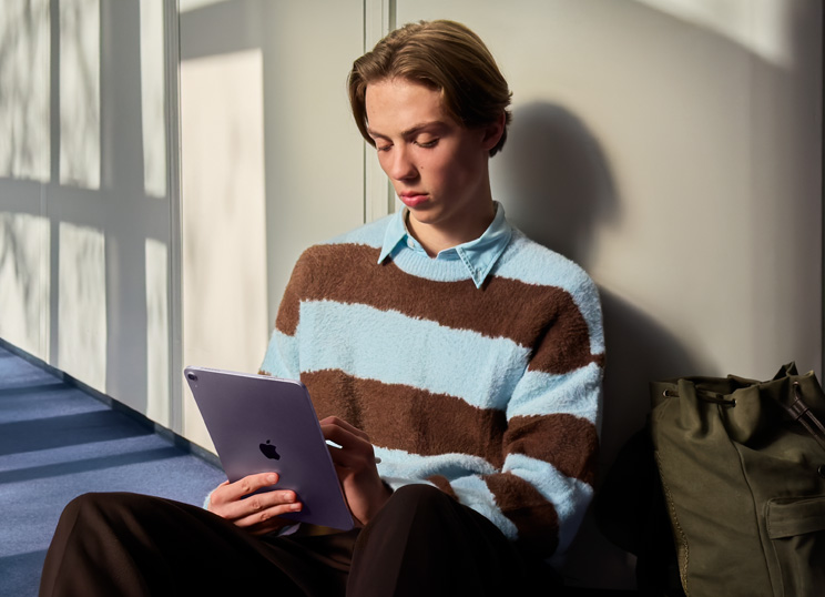 Eine Person sitzt in einem lichtdurchfluteten Raum auf dem Boden und benutzt ein iPad und einen Apple Pencil.
