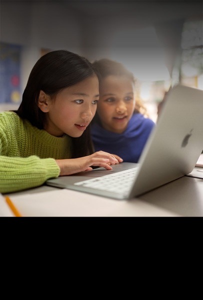 Due giovani studenti a una scrivania che guardano un MacBook con grande attenzione mentre collaborano in classe