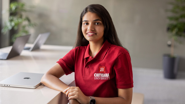 Nishtha Tandon duduk di belakang meja dengan MacBook tertutup di sampingnya, tersenyum ke kamera.