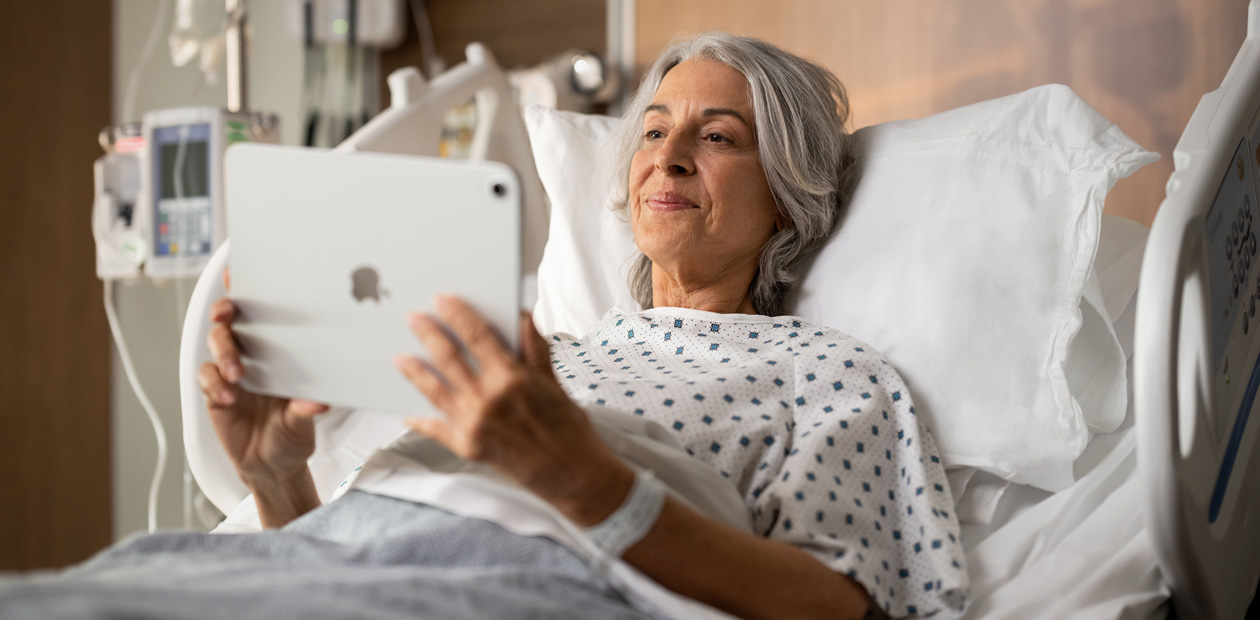 病院のベッドに横たわりiPadを見ている女性患者